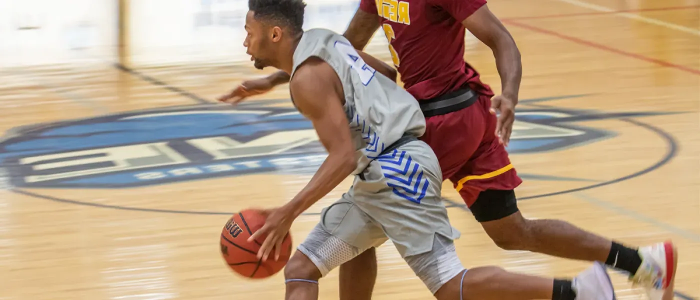 A U N E basketball player dribbles the ball across the U N E court during a game